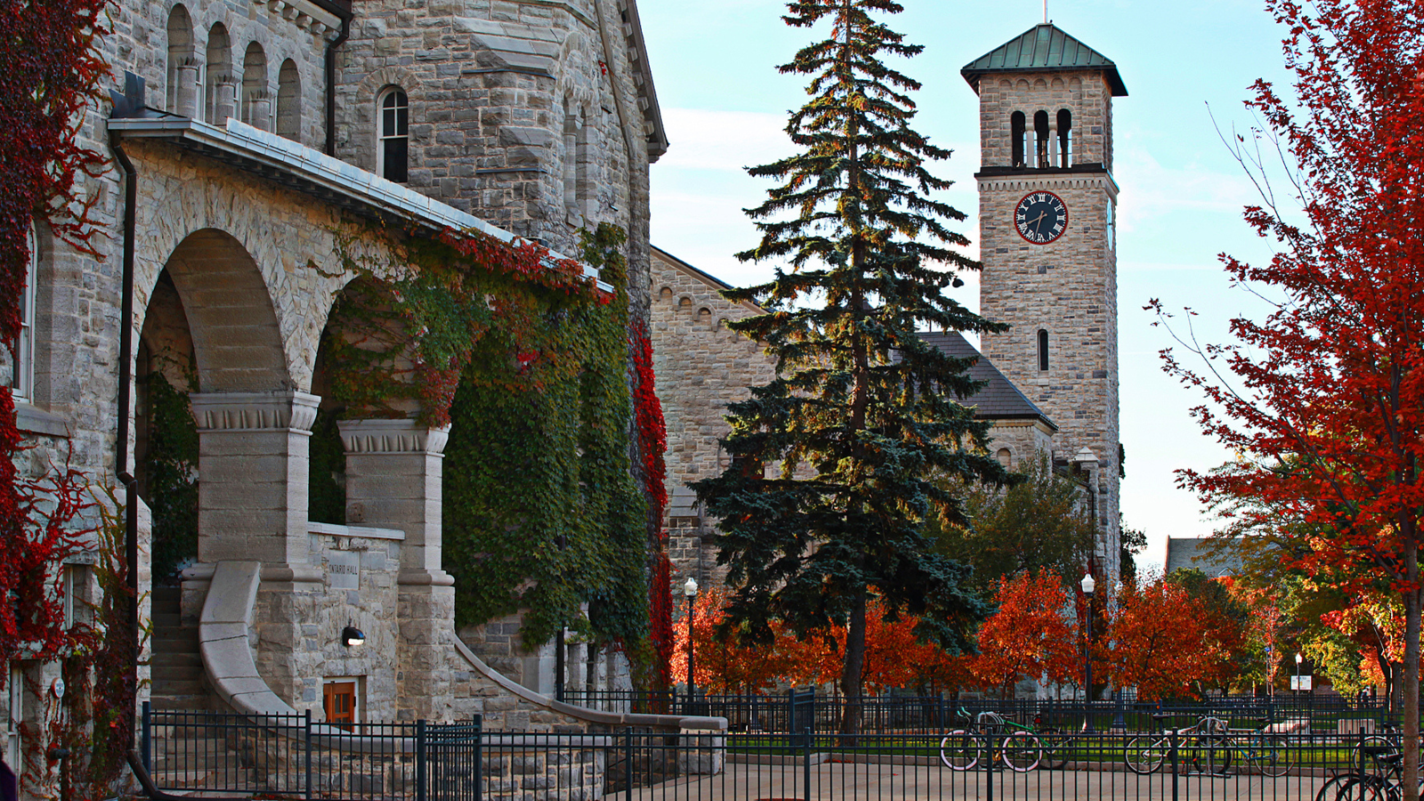 Photo of Queen's campus, showing picturesque limestone brick university buildings, with a view of the Grant Hall clock tower in the background to the right. 