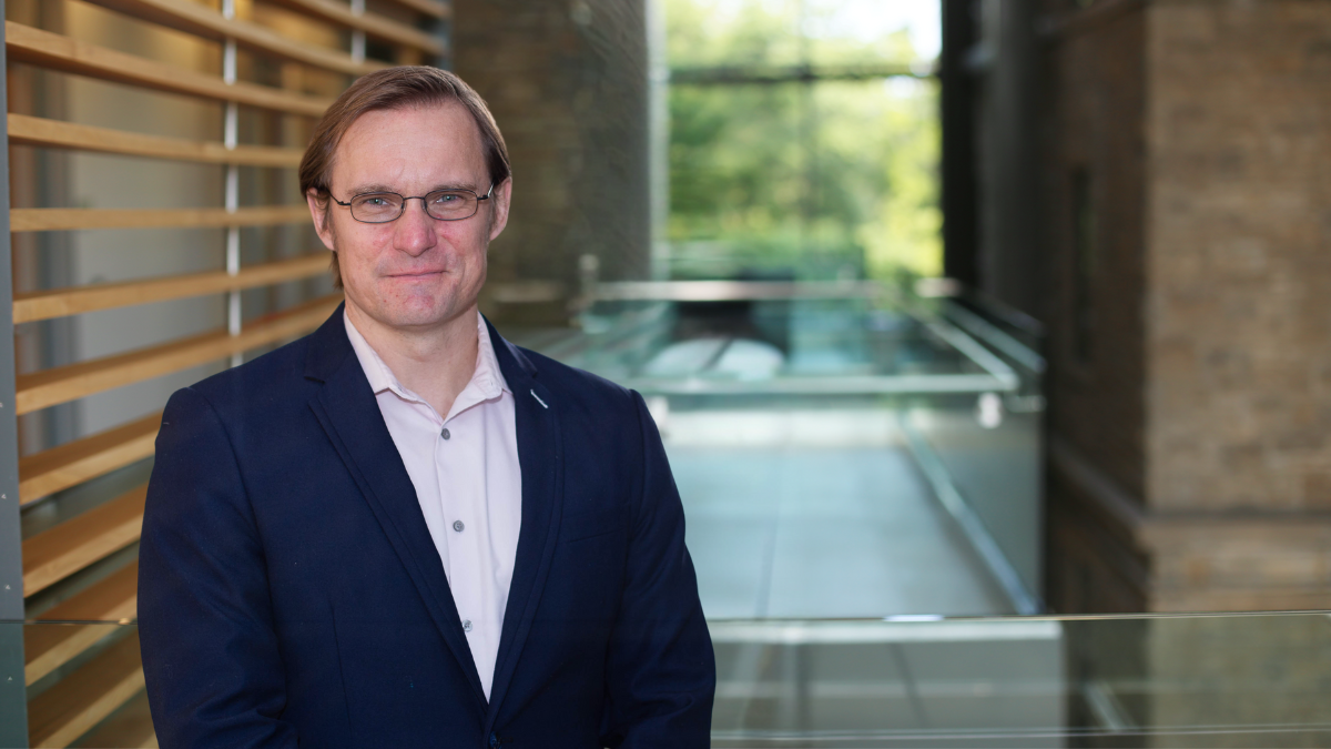 photo of Rylan Egan wearing glasses and smiling at the camera while wearing a white dress shirt and navy jacket