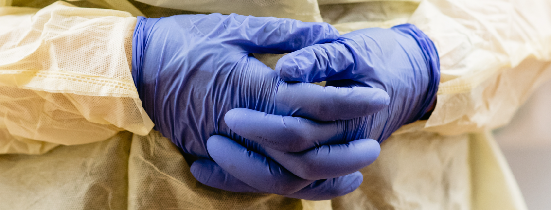 close cropped photo of health professional's hands clasped together, wearing full personal protection equipment  