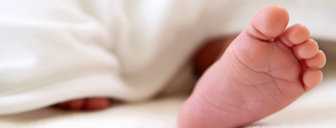 image of a newborn baby's foot peeking out from undernear a white blanket