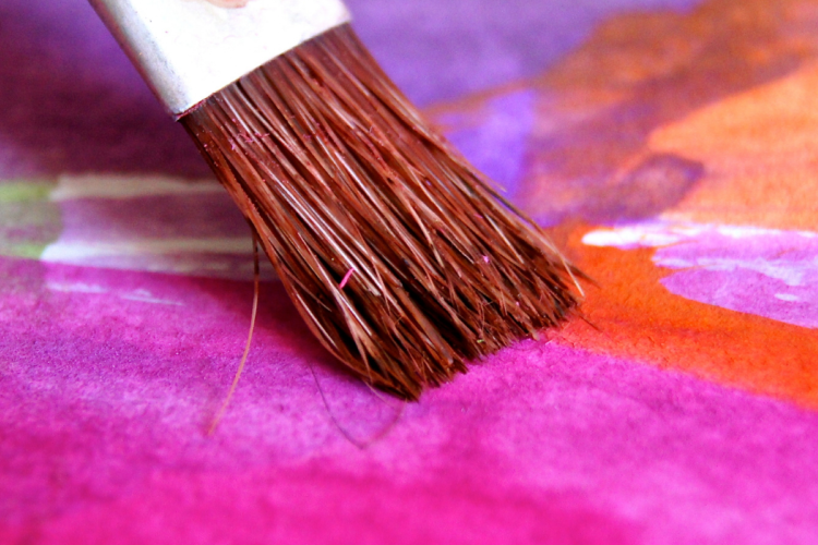 a paintbrush moving across a pink and purple water colour sketch