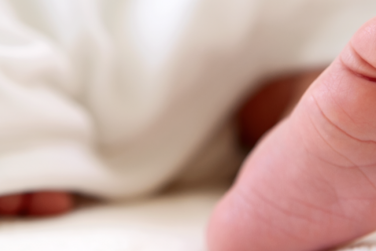 image of a newborn baby's foot peeking out from undernear a white blanket