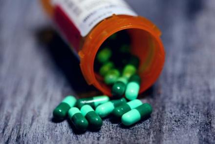 Green pills spilling from orange medication bottle