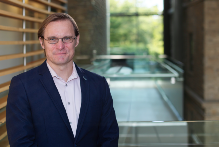 photo of Rylan Egan wearing glasses and smiling at the camera while wearing a white dress shirt and navy jacket