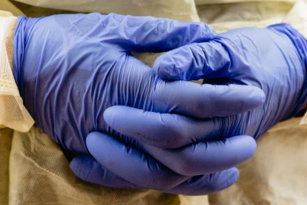 close cropped photo of health professional's hands clasped together, wearing full personal protection equipment  