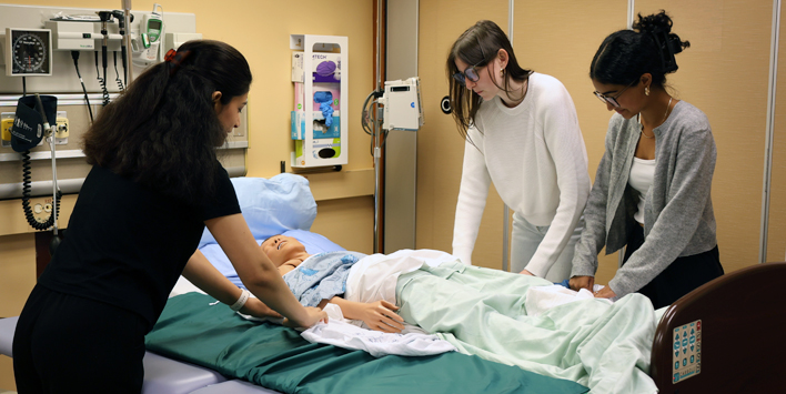 Nursing students practise patient care with a simulation mannequin in a clinical lab.