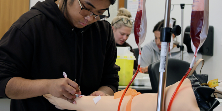 A nursing student practises an injection technique on a training model in a simulation lab.