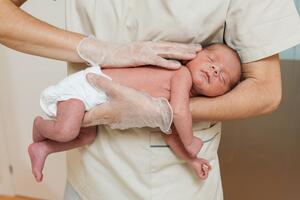 a newborn lying on their stomach, being held by a healthcare provider in ivory scrubs and wearing clear gloves.